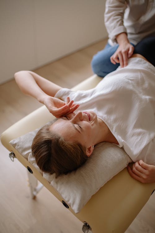 Massage training scene showing a relaxed female client lying on a massage table in a calmly arranged therapy room, emphasizing comfort and professional setup.